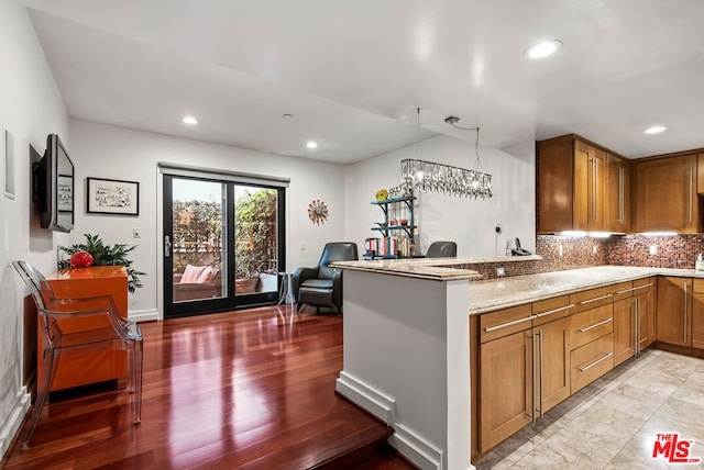 kitchen featuring light stone countertops, an inviting chandelier, decorative backsplash, hanging light fixtures, and kitchen peninsula