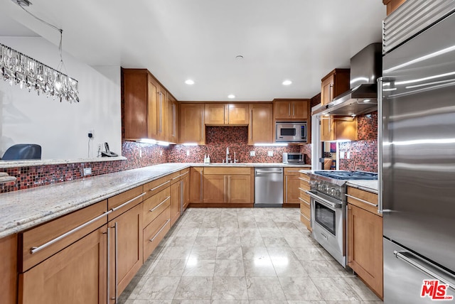 kitchen featuring decorative backsplash, sink, built in appliances, wall chimney exhaust hood, and light stone counters