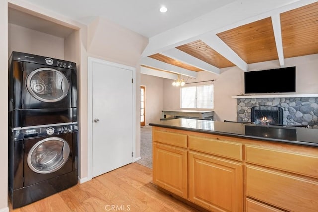 kitchen featuring stacked washer / drying machine, a fireplace, beam ceiling, light hardwood / wood-style flooring, and a chandelier