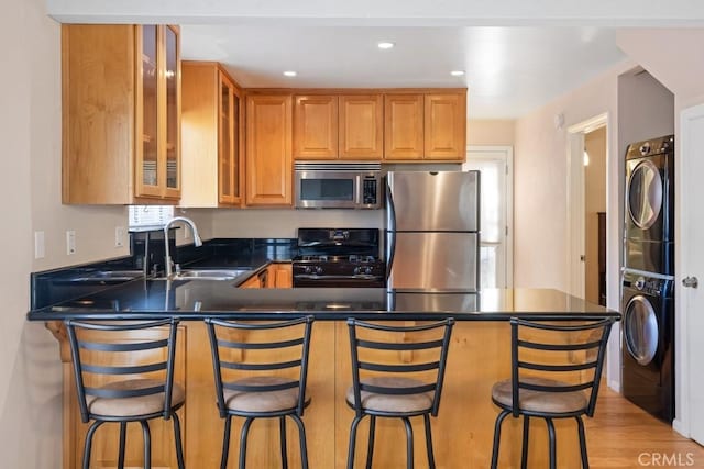 kitchen featuring a breakfast bar, kitchen peninsula, sink, stacked washing maching and dryer, and appliances with stainless steel finishes