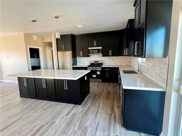 kitchen featuring decorative light fixtures, backsplash, a kitchen island, sink, and appliances with stainless steel finishes