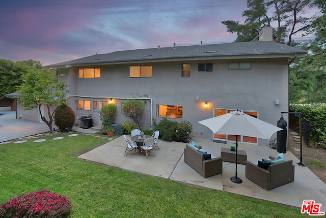 back house at dusk featuring a lawn, a patio area, and outdoor lounge area