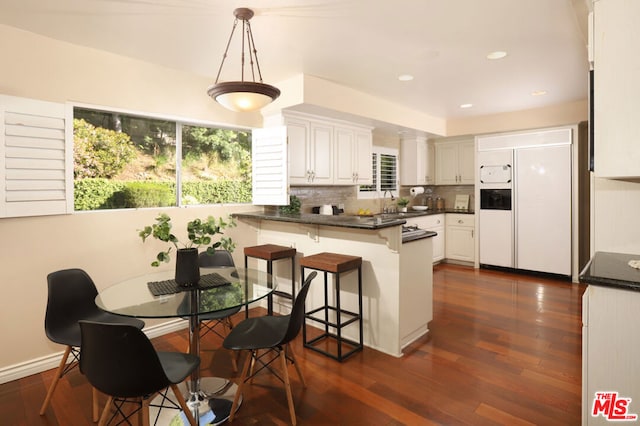 kitchen featuring white cabinetry, kitchen peninsula, paneled built in fridge, pendant lighting, and a breakfast bar