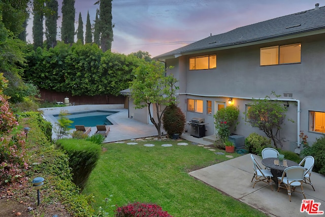 back house at dusk featuring a yard and a patio