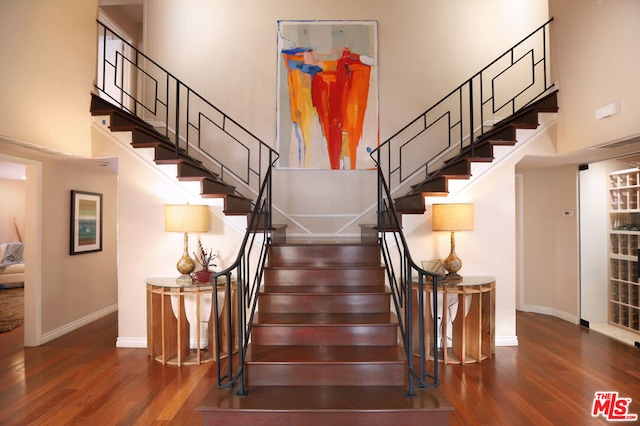 staircase with a towering ceiling and hardwood / wood-style flooring