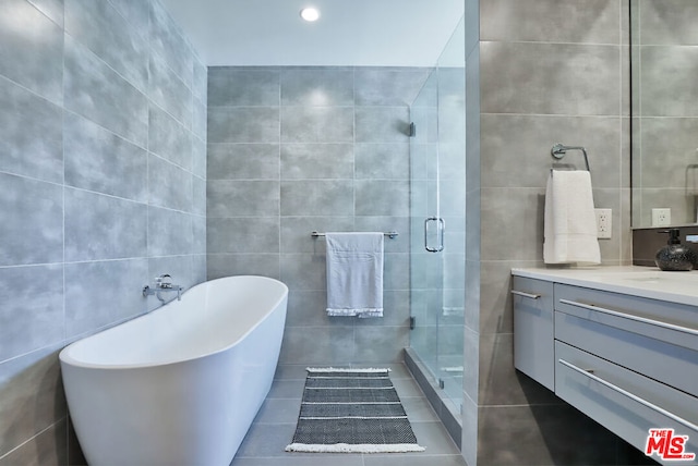 bathroom with plus walk in shower, tile patterned flooring, tile walls, and vanity