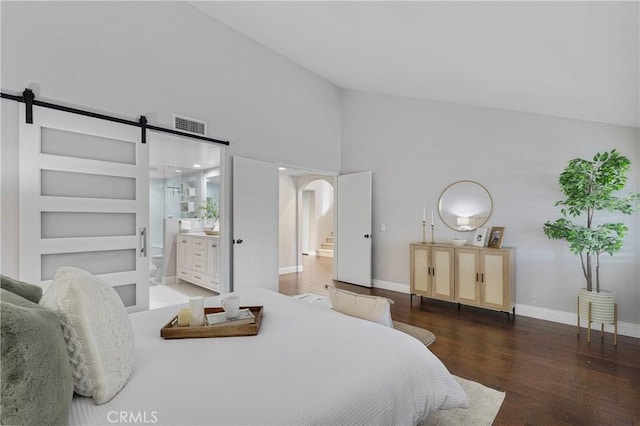 bedroom featuring a barn door, dark hardwood / wood-style flooring, a high ceiling, and connected bathroom