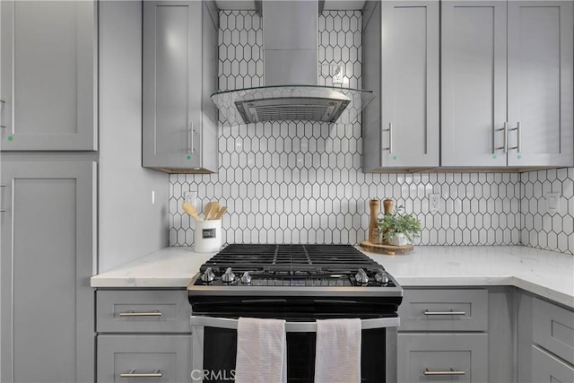 kitchen featuring stainless steel range with gas cooktop, gray cabinets, wall chimney exhaust hood, and tasteful backsplash