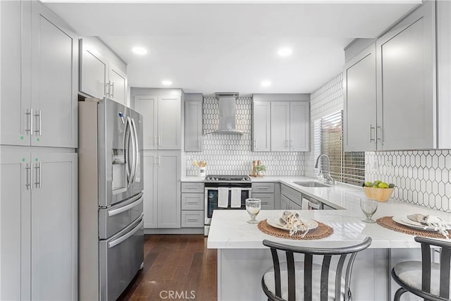 kitchen featuring wall chimney range hood, a breakfast bar, kitchen peninsula, sink, and stainless steel appliances