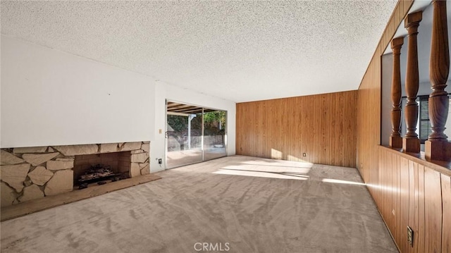 unfurnished living room with a textured ceiling, light colored carpet, wood walls, and a stone fireplace