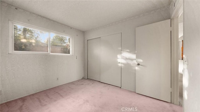 unfurnished bedroom featuring a textured ceiling, a closet, and light colored carpet