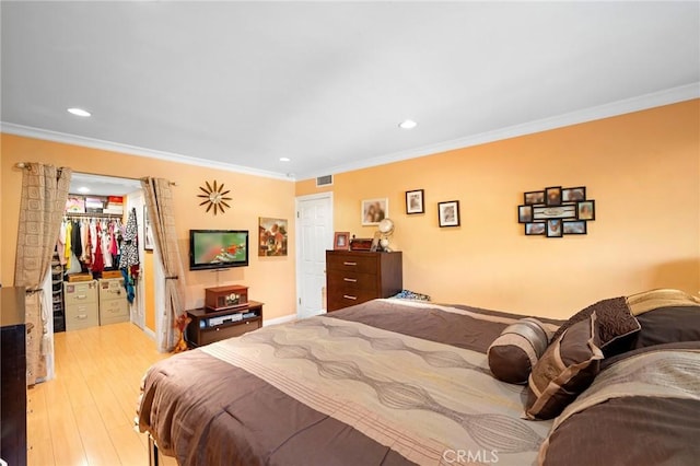 bedroom featuring light hardwood / wood-style floors, a spacious closet, a closet, and crown molding