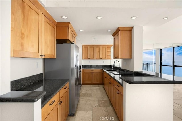 kitchen featuring stainless steel refrigerator with ice dispenser, sink, kitchen peninsula, and dark stone counters