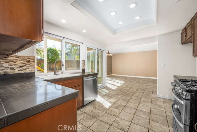 kitchen with light tile patterned floors, stainless steel appliances, a raised ceiling, a notable chandelier, and crown molding