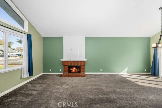 unfurnished living room featuring lofted ceiling, a healthy amount of sunlight, a fireplace, and dark colored carpet