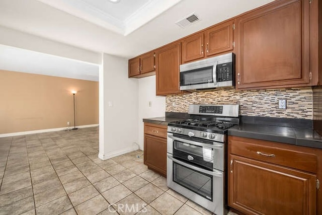 kitchen with light tile patterned flooring, appliances with stainless steel finishes, decorative backsplash, and a raised ceiling