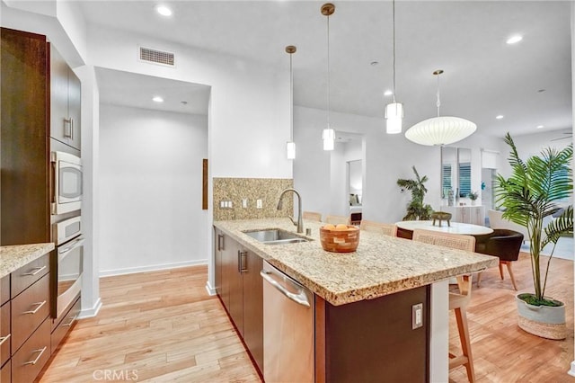 kitchen featuring appliances with stainless steel finishes, decorative backsplash, sink, light hardwood / wood-style flooring, and pendant lighting