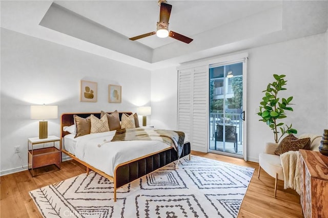 bedroom with access to outside, light hardwood / wood-style flooring, a raised ceiling, and ceiling fan