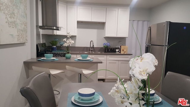 kitchen with white cabinets, range, wall chimney exhaust hood, sink, and stainless steel fridge