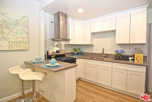 kitchen with stainless steel gas range oven, sink, white cabinetry, light hardwood / wood-style flooring, and wall chimney exhaust hood