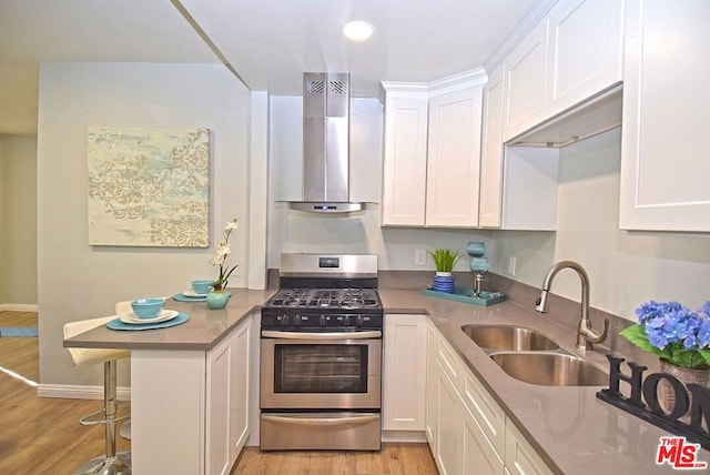 kitchen featuring wall chimney exhaust hood, white cabinets, stainless steel range with gas stovetop, and sink