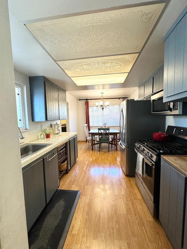 kitchen with sink, an inviting chandelier, stainless steel appliances, and light hardwood / wood-style flooring