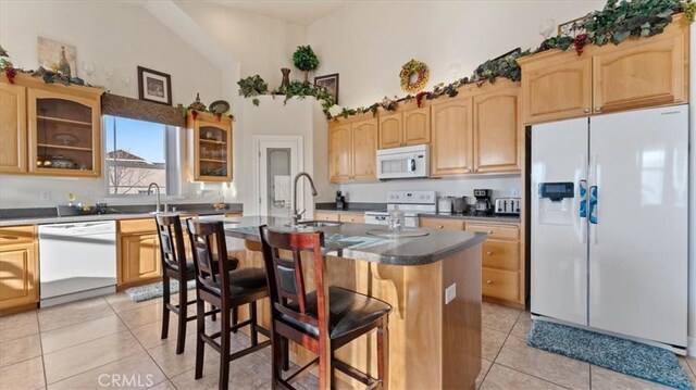 kitchen featuring a center island with sink, a breakfast bar area, glass insert cabinets, a sink, and white appliances