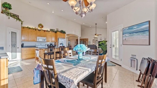 dining area featuring arched walkways, high vaulted ceiling, light tile patterned flooring, recessed lighting, and ceiling fan with notable chandelier