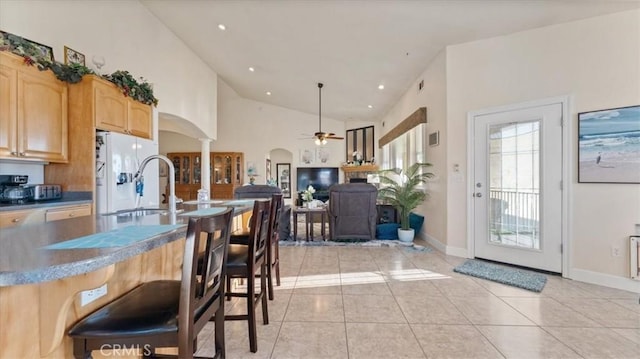 kitchen featuring arched walkways, decorative light fixtures, light brown cabinetry, open floor plan, and white fridge with ice dispenser