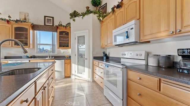 kitchen with light tile patterned floors, dark countertops, glass insert cabinets, a sink, and white appliances