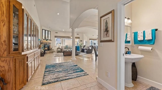 entryway with arched walkways, a stone fireplace, light tile patterned flooring, baseboards, and ornate columns