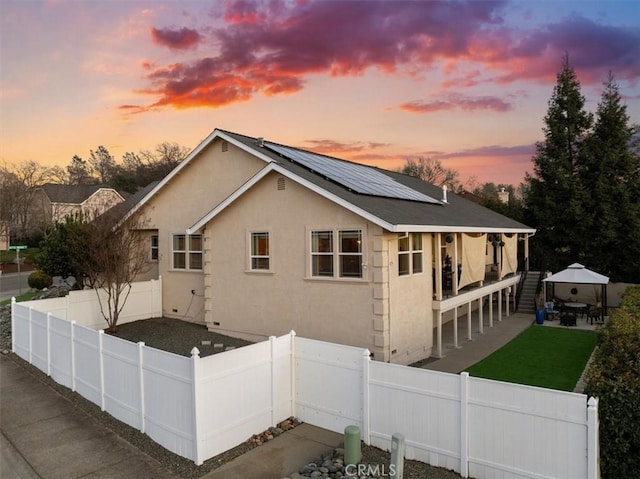 view of home's exterior with a fenced backyard, roof mounted solar panels, metal roof, and stucco siding