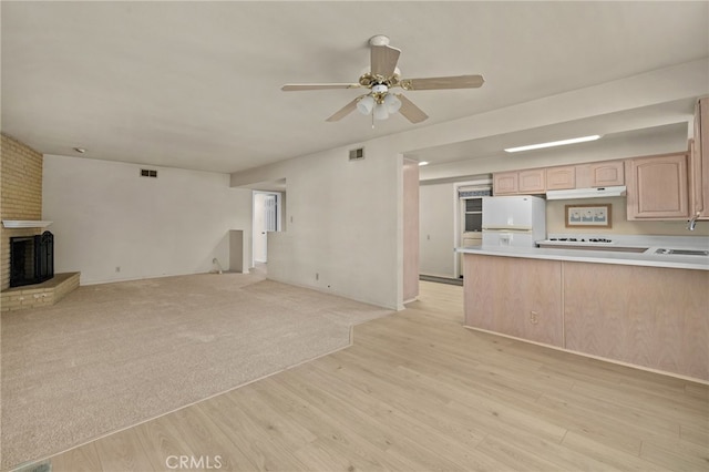 unfurnished living room featuring ceiling fan, light hardwood / wood-style flooring, a brick fireplace, and sink