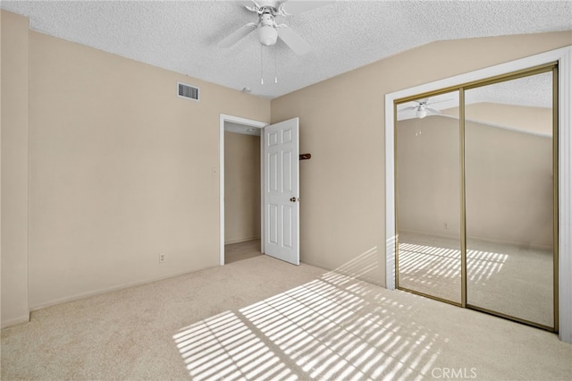 unfurnished bedroom featuring a textured ceiling, a closet, vaulted ceiling, ceiling fan, and light colored carpet