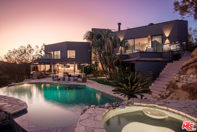 pool at dusk featuring a patio area, a hot tub, and an outdoor hangout area