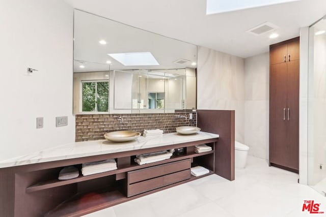 bathroom with toilet, vanity, a skylight, and tasteful backsplash