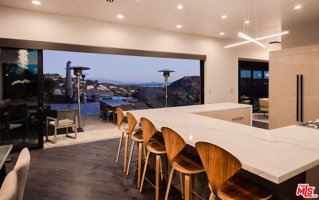 kitchen featuring a spacious island, dark hardwood / wood-style floors, a mountain view, a breakfast bar, and light stone counters