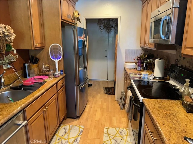 kitchen featuring light hardwood / wood-style floors, decorative backsplash, sink, stainless steel appliances, and light stone counters