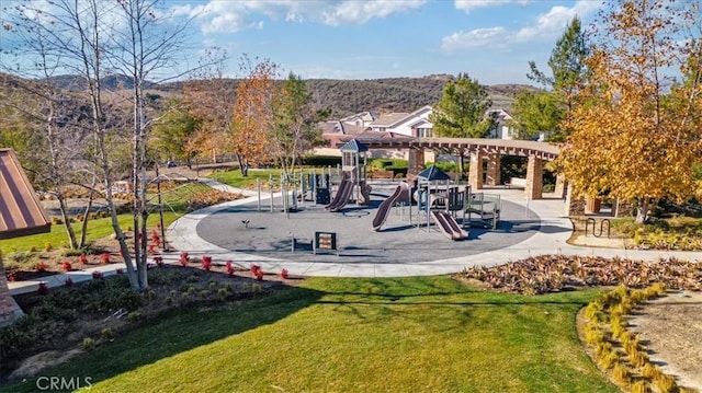 surrounding community featuring a playground, a lawn, and a mountain view