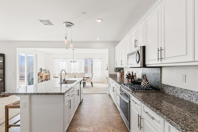 kitchen with white cabinetry, appliances with stainless steel finishes, a kitchen island with sink, pendant lighting, and sink