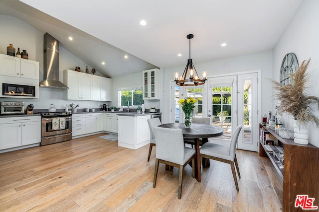 kitchen featuring pendant lighting, stainless steel range oven, wall chimney exhaust hood, a notable chandelier, and light hardwood / wood-style flooring