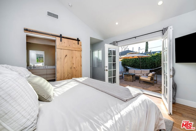 bedroom with french doors, vaulted ceiling, a barn door, and light wood-type flooring