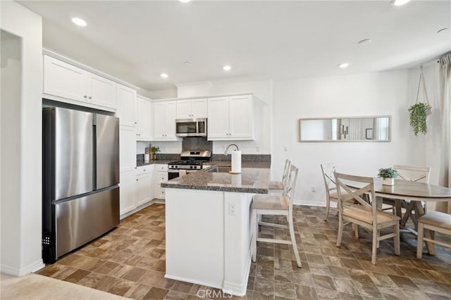 kitchen with white cabinetry, sink, stainless steel appliances, and dark stone countertops