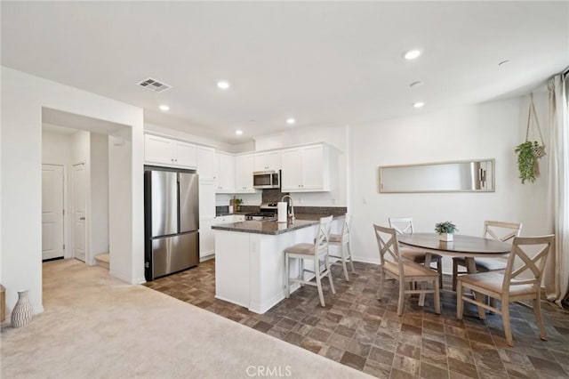 kitchen with white cabinetry, stainless steel appliances, a breakfast bar, and dark stone countertops