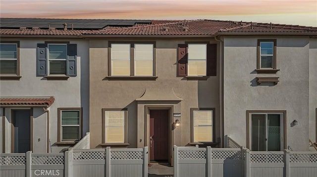 view of property with a tile roof, fence, and stucco siding