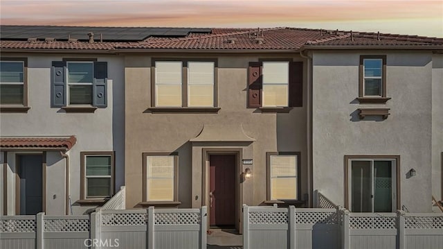 multi unit property with a tiled roof, fence, solar panels, and stucco siding