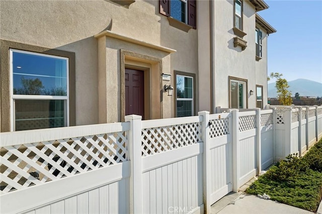 view of exterior entry with fence, a mountain view, and stucco siding