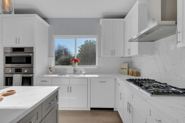 kitchen featuring white cabinetry, decorative backsplash, sink, stainless steel appliances, and wall chimney exhaust hood