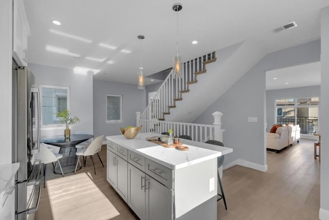 kitchen featuring a center island, decorative light fixtures, stainless steel refrigerator, light stone counters, and light hardwood / wood-style flooring