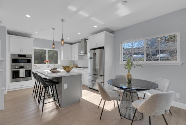 kitchen with pendant lighting, white cabinets, appliances with stainless steel finishes, a center island, and wall chimney exhaust hood